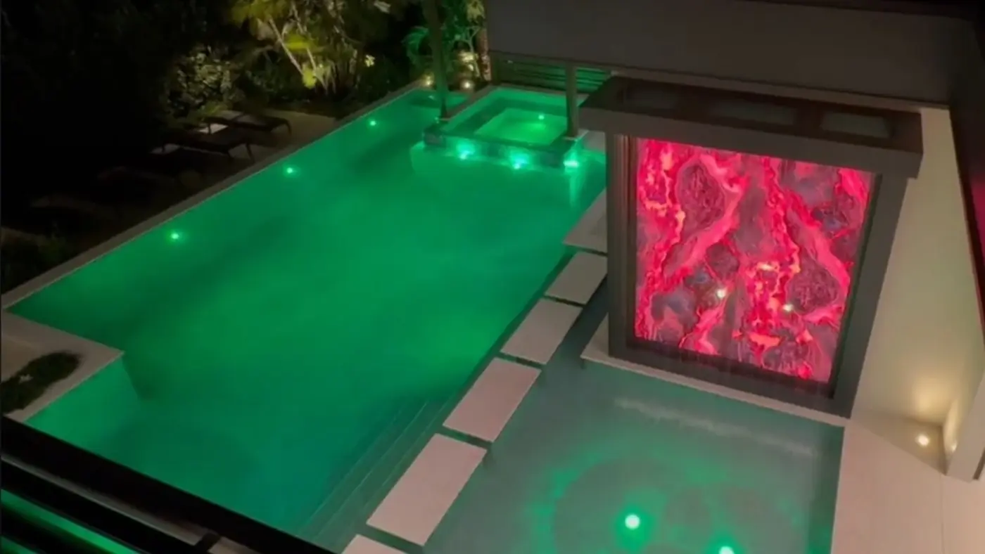 Red illuminated glass feature wall beside a pool by Dyer Design Glassworks