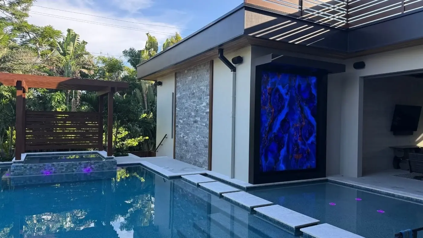Blue illuminated glass wall beside a swimming pool by Dyer Design Glassworks